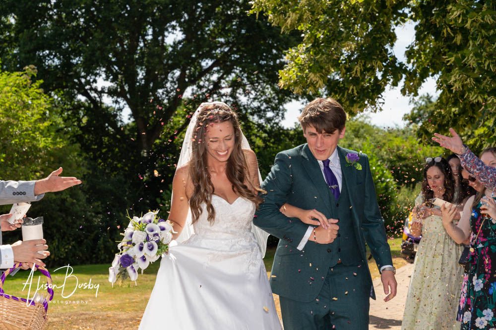 Bride and groom walk through confetti at tipi wedding in Oxfordshire.