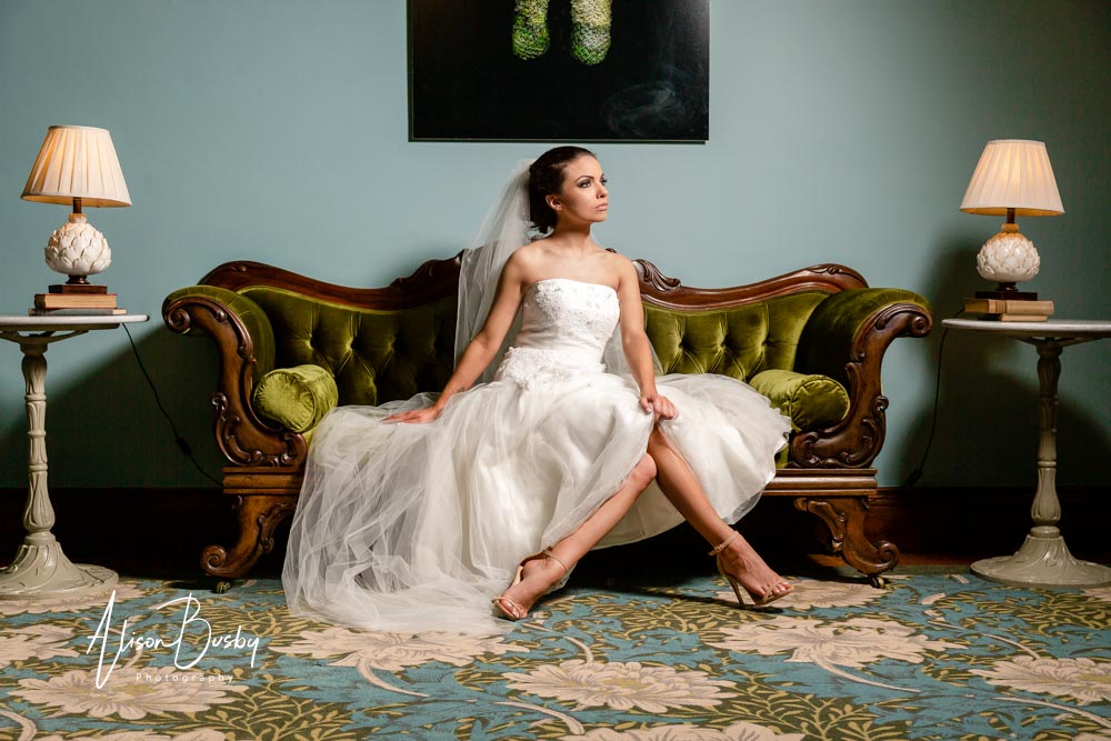 Eynsham Hall wedding photographer. Bride on green sofa at Eynsham Hall in Oxfordshire