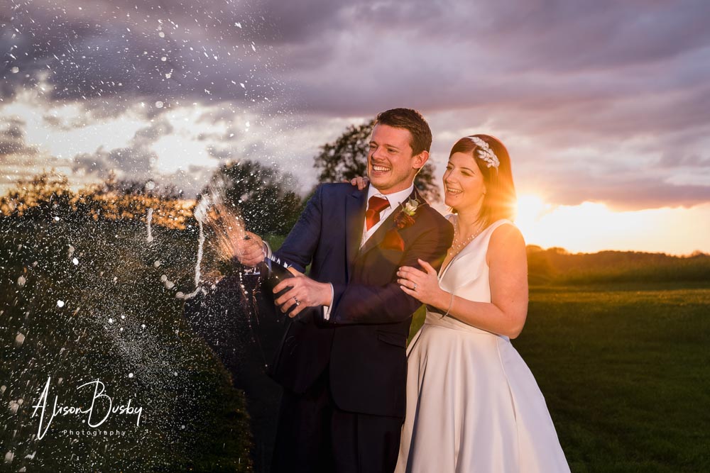 Bride and groom with champagne spray at sunset. Oxfordshire wedding photographer
