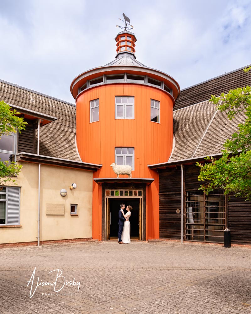 Sheepdrove organic farm. Bride and groom in front of farm entrance. Orange tower with sheep weather vane