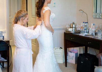 How to choose a wedding photographer in the UK. Bride and bridesmaid buttoning up wedding gown.