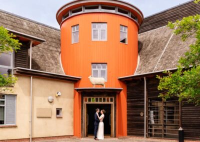 Sheepdrove Organic Farm in Berkshire. Bride and groom under orange grain tower.