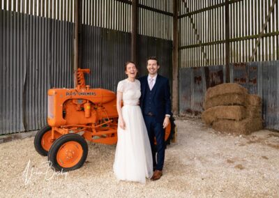 Sheepdrove Organic Farm in Berkshire. Bride and groom next to Allis Chalmers orange tractor