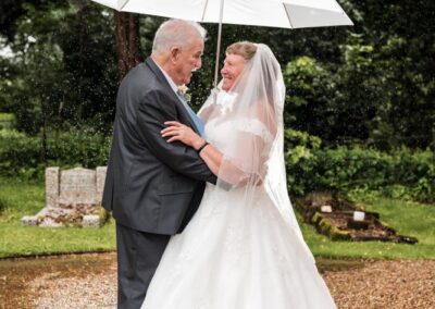 Wedding photography for older couples. Bride and groom under umbrella outside church.