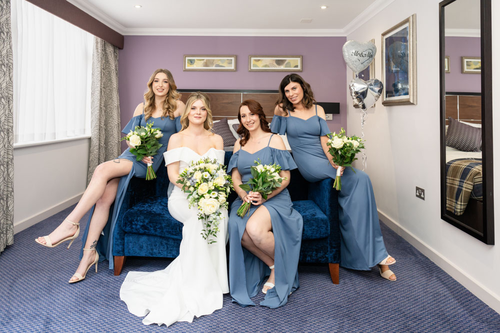 Bride and bridesmaids seated on blue sofa before wedding ceremony at the Bull Hotel in Gerrards Cross