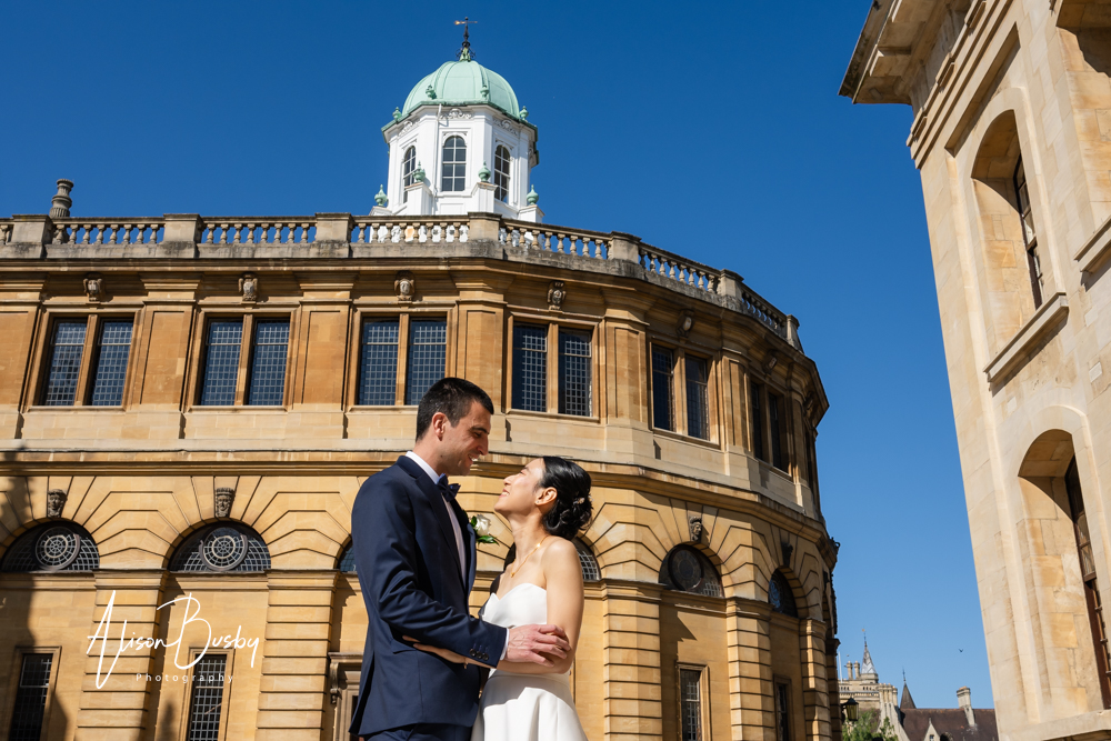 Bride and groom embrace in front of Sheldonian Theatre Oxford. By Bodleian Library wedding photographer.