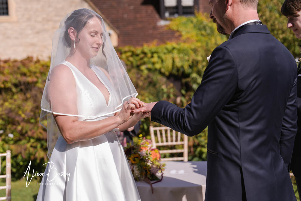 Bride and groom exchange rings during outdoor wedding ceremony at Le Manoir aux Quat'Saisons. Photo by Alison Busby