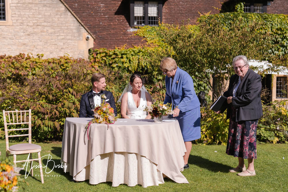 Bride and groom complete paperwork after outdoor wedding ceremony at Le Manoir aux Quat'Saisons. Photo by Alison Busby