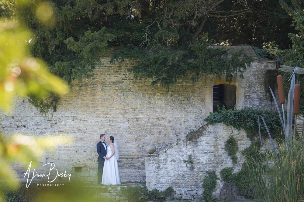 Bride and groom on steps next to 15th Century pond with Le Manoir wedding photographer Alison Busby
