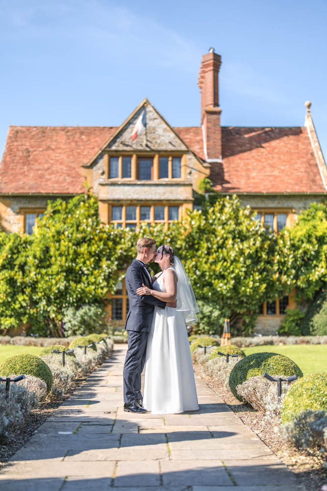 Le Manoir wedding photographer with bride and groom as they kiss on lavender path in front of the hotel