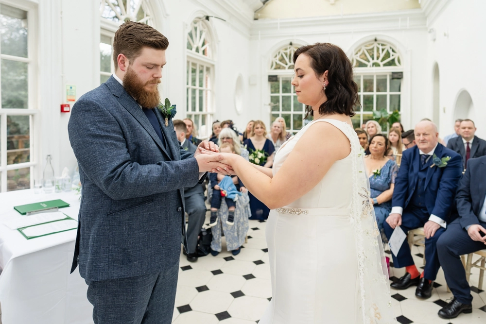 Bride and groom exchanging rings during ceremony in conservatory. Hunton Park wedding photographer.