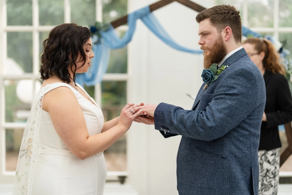 Bride and groom exchanging rings during ceremony in conservatory. Hunton Park wedding photographer.