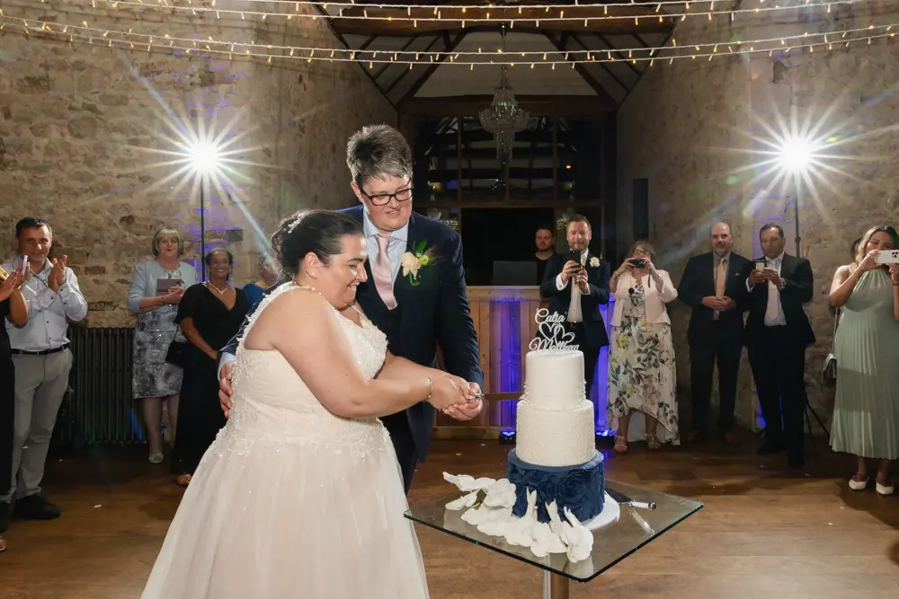 Notley Abbey Wedding photographer. Bride and groom cut the cake in monk's refectory.
