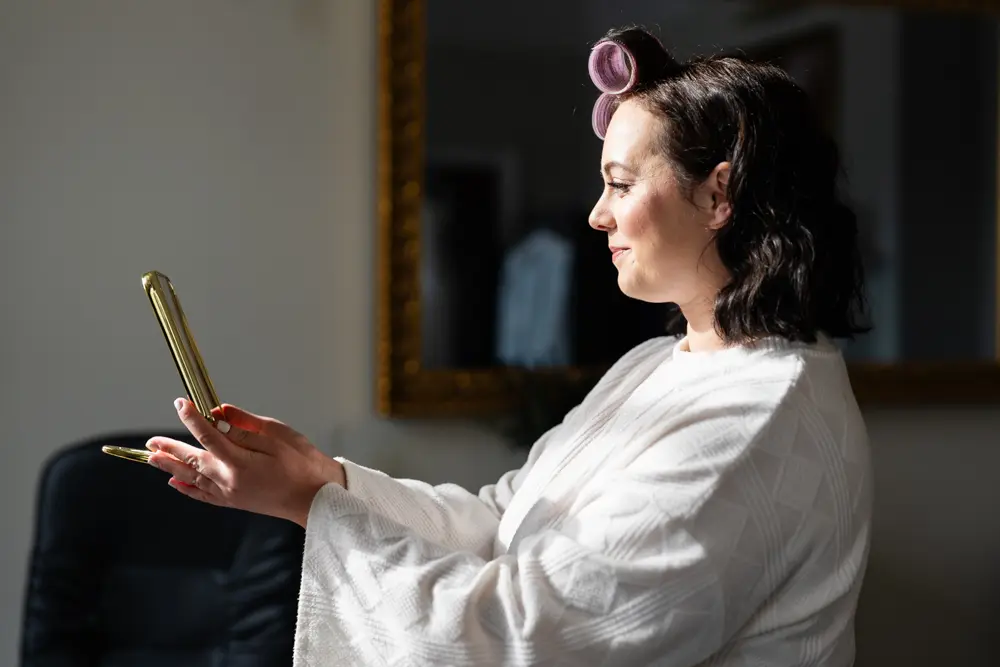 Hunton Park wedding photos of bride looking at makeup in morning sunlight