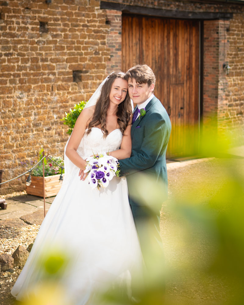 Bride and groom next to barn at Dovecote events by Oxford wedding photographer.