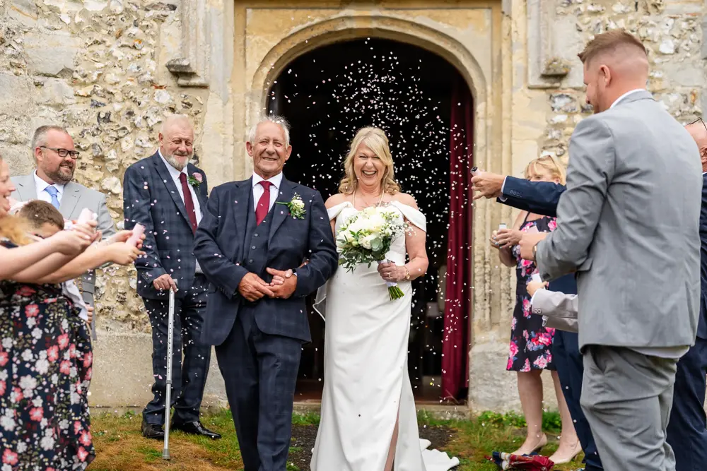 Bride and groom in confetti tunnel leaving wedding ceremony at St Boltoph church. Bradenham wedding photographer Buckinghamshire.