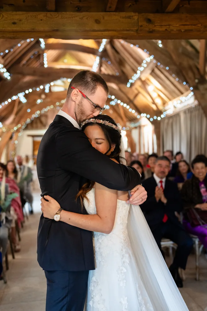 Notley Tythe Barn wedding photos. Bride and groom embrace at the end of wedding ceremony.