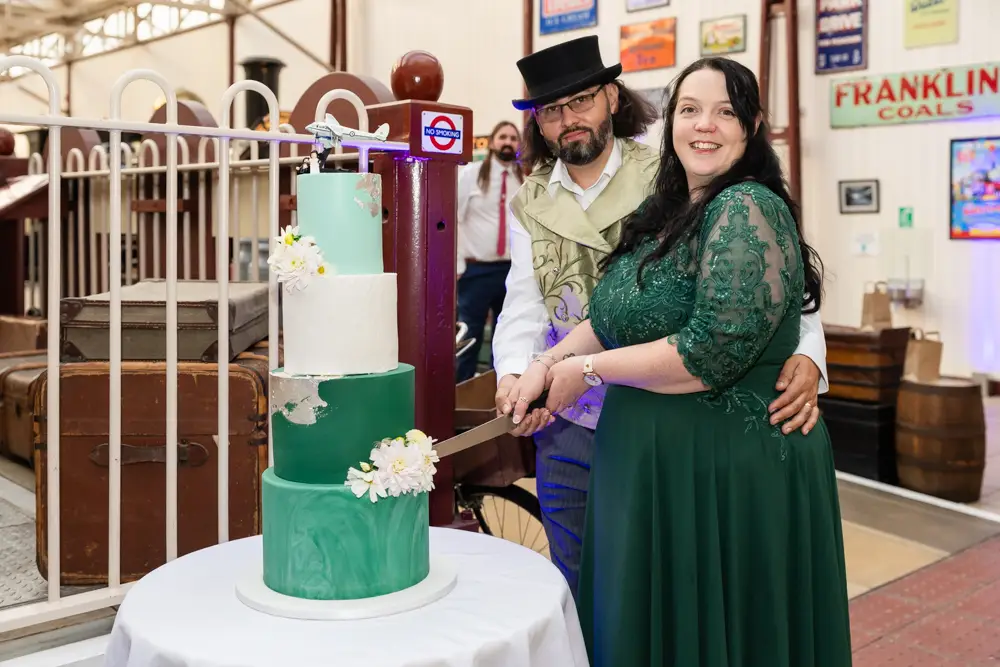 Buckinghamshire Railway Centre Wedding Photographer. Bride and groom cut wedding cake in main hall.