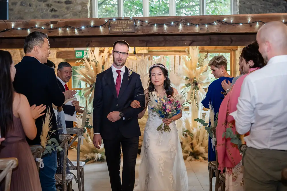 Notley Tythe Barn Wedding Photography. Bride and groom leaving wedding ceremony in barn.