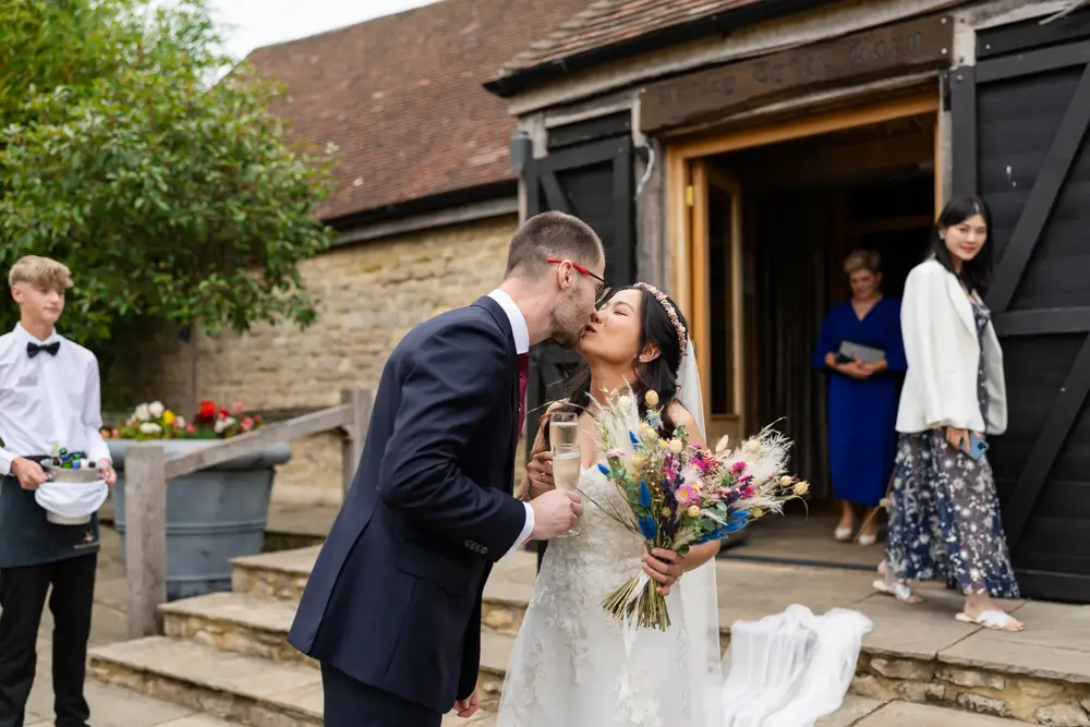 Notley Tythe Barn Wedding Photography. Bride and groom kiss outside barn.