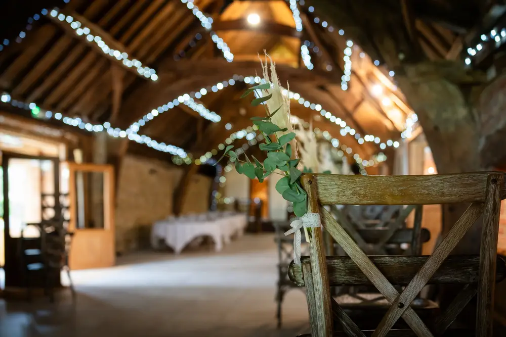 Notley Tythe Barn Wedding Photography. Chair decorations with fairy light bokeh of barn