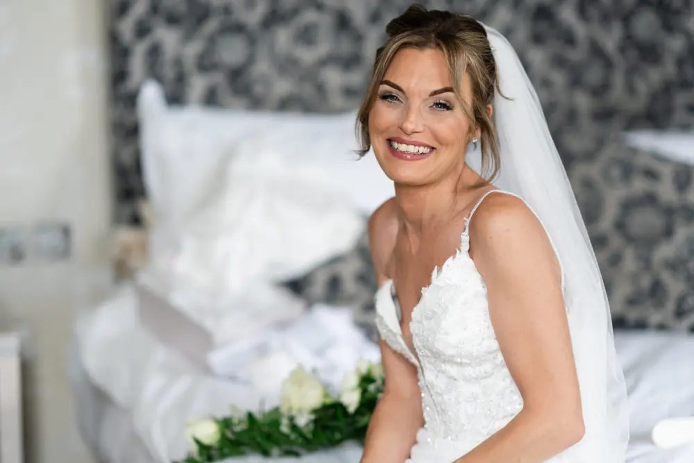 Stoke Place wedding photographer. Bride seated on bed in Alexandra suite