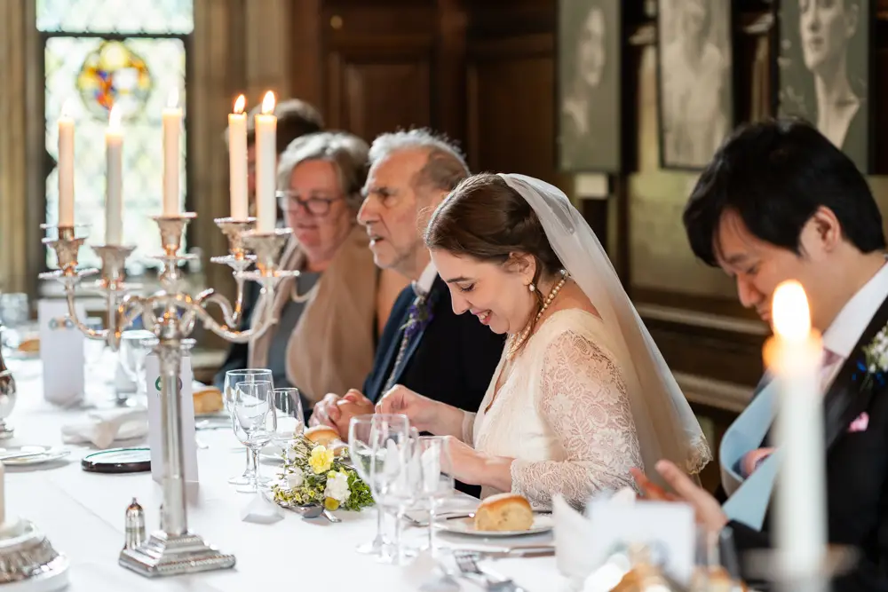 Lincoln College Oxford wedding photographer. Bride bows her head during her father's speech during wedding breakfast in the dining room.