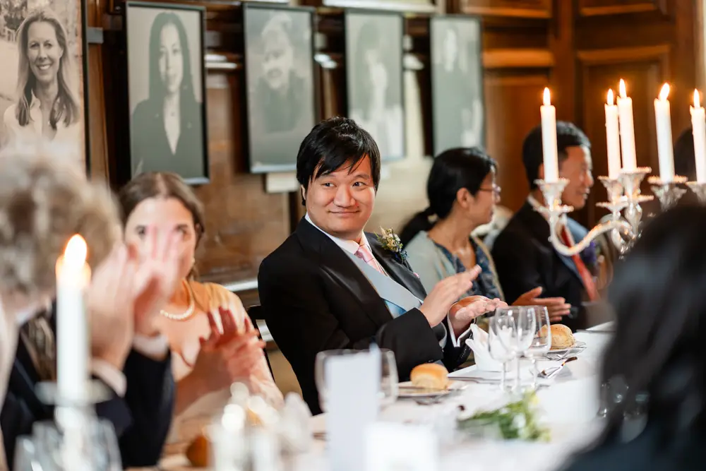 Lincoln College Oxford wedding photographer. Groom claps at the end of father of the bride's speech during wedding breakfast in the dining room.