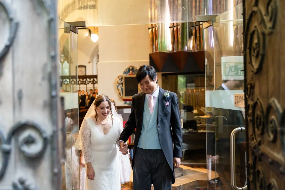 St Mary Magdalen Oxford Wedding Photographer. Bride and groom walking through glass doors of church after their wedding ceremony.
