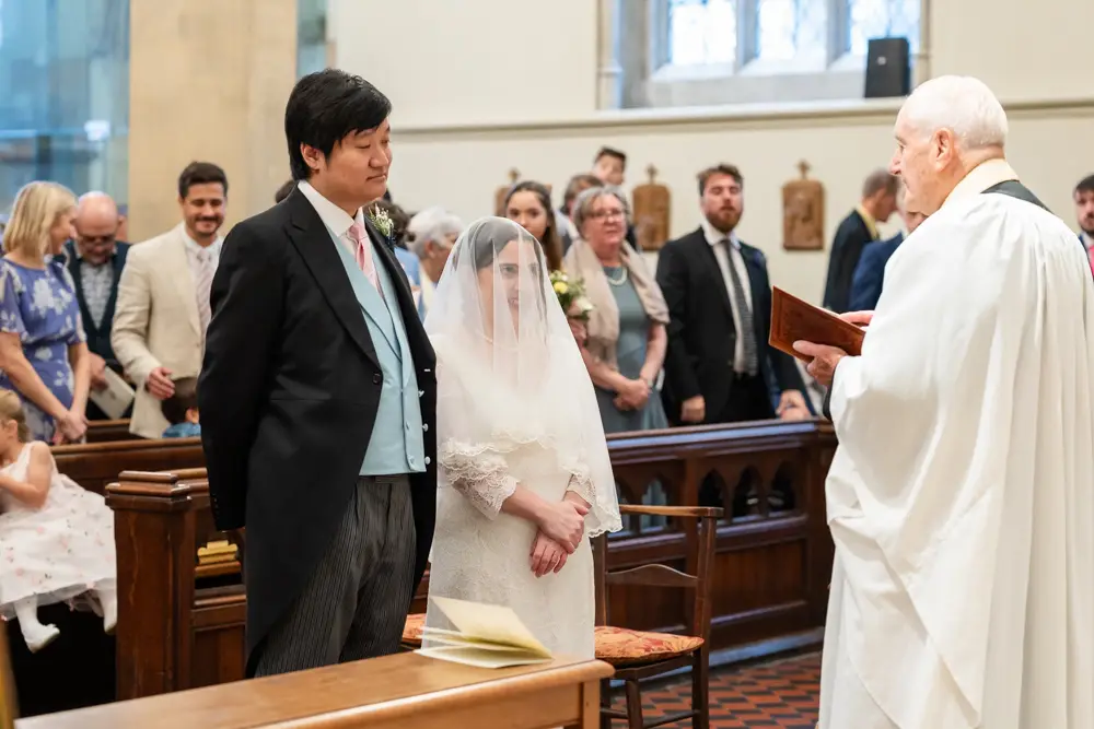 St Mary Magdalen Oxford Wedding Photographer. Bride and groom face the priest at the start of the wedding ceremony.