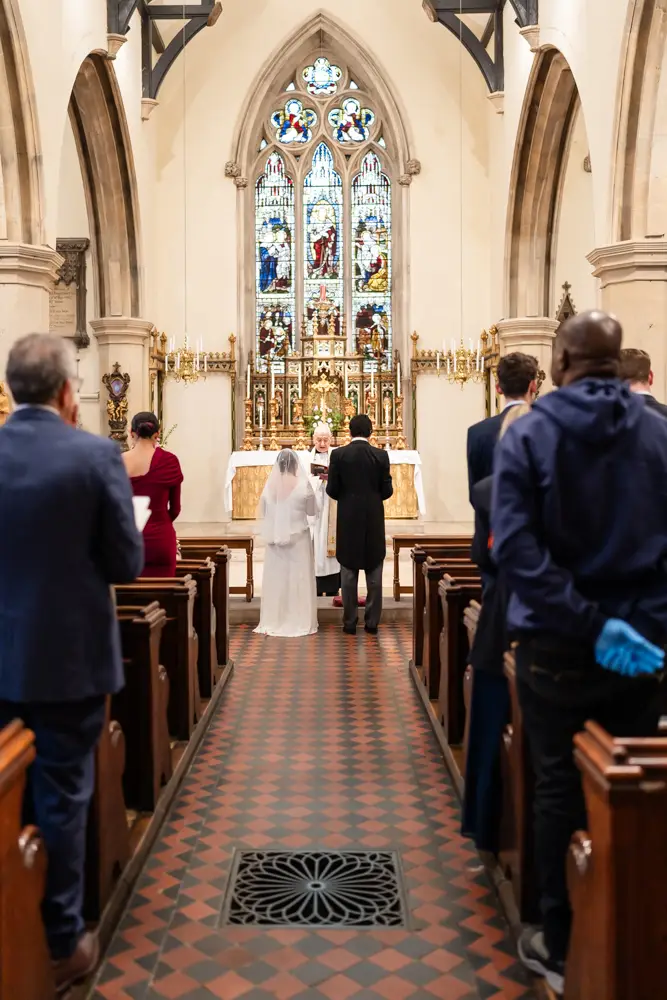 St Mary Magdalen Oxford Wedding Photographer. view from the back of the church of the Bride and groom as they face the priest during their wedding ceremony.