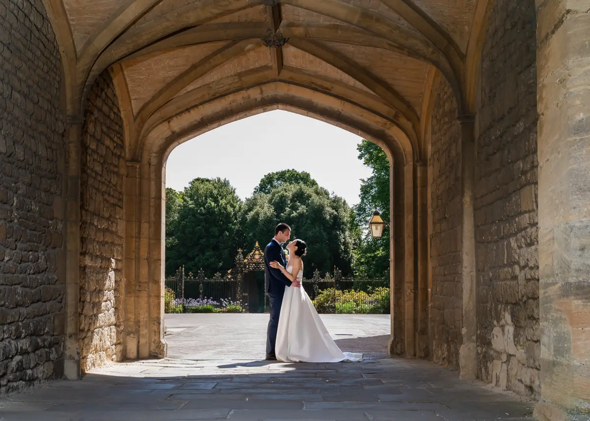Bride and groom under arch at New College with garden in background. Oxford wedding photographer.