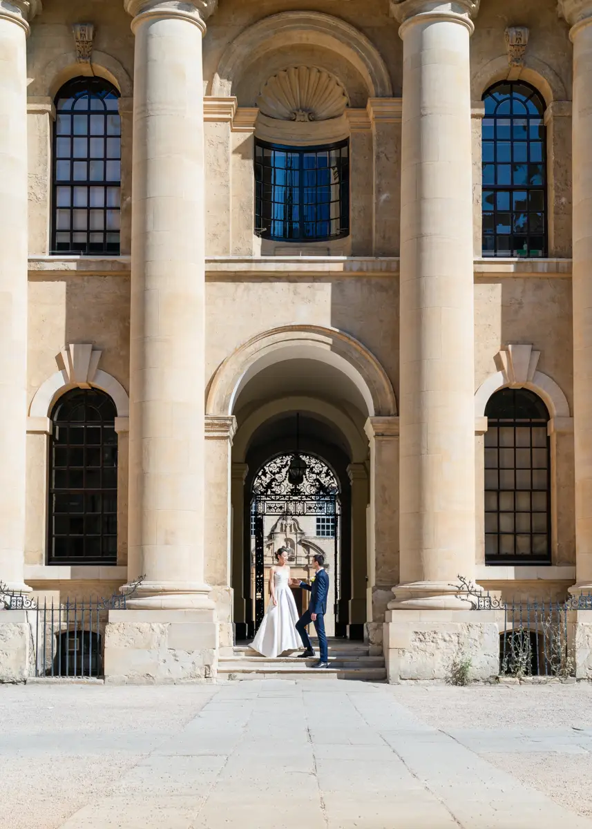 Bride and groom on steps of Clarendon Building in Old Schools Quad. Oxford wedding photographer.