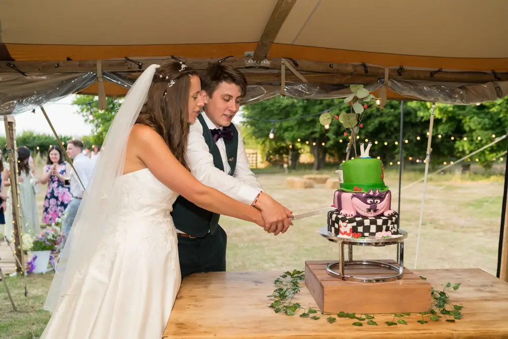 Oxfordshire Wedding Photographer. Bride and groom cut cake at Dovecote Events.