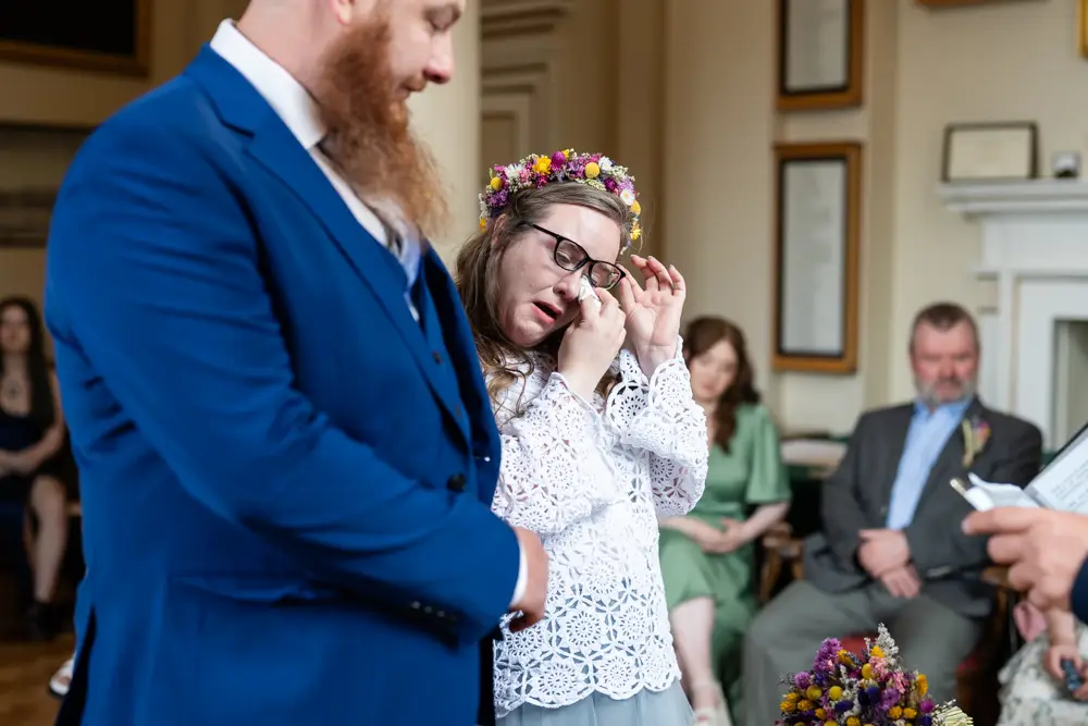 Bride sheds a tear for absent friends during ceremony at Woodstock Town Hall in Oxfordshire