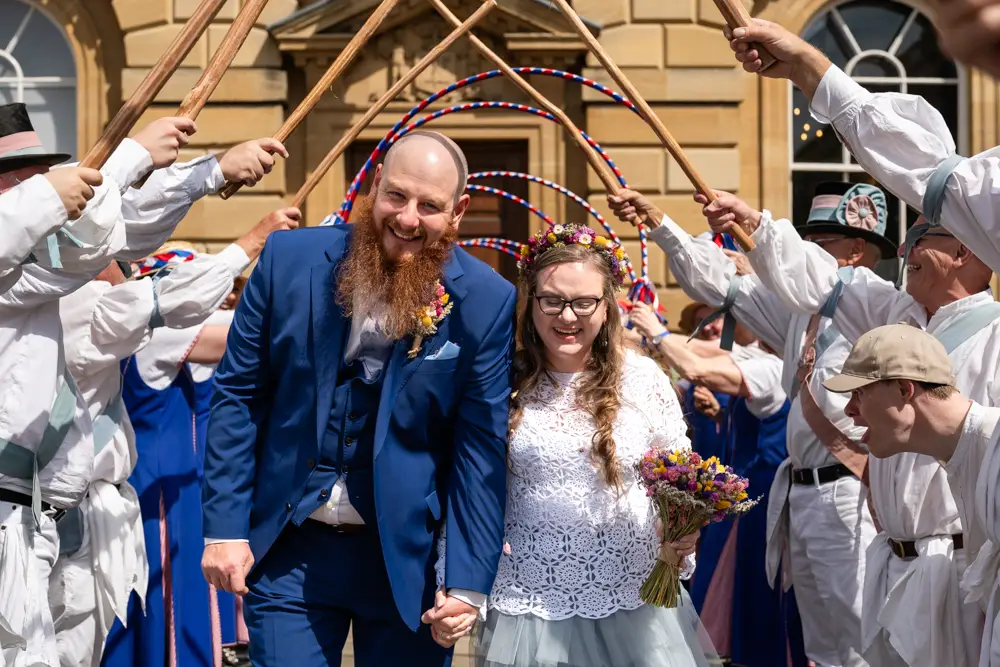 Woodstock wedding photographer. Bride and groom laughing as hey walk under Morris Dancer's canopy