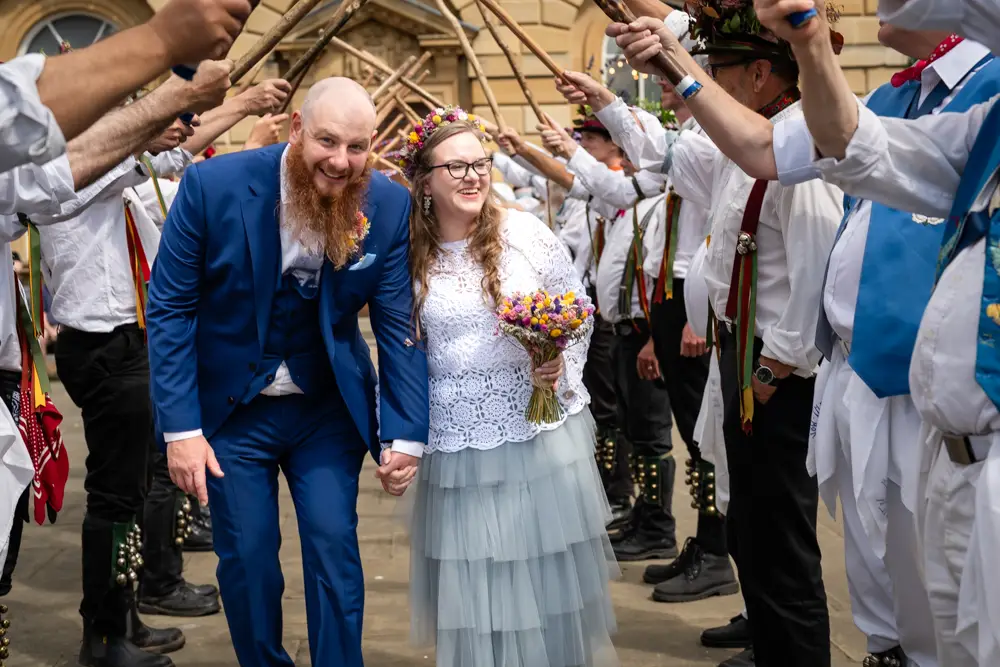 Woodstock wedding photographer. Bride and groom laughing as they walk under Morris Dancer's canopy outside the town hall.