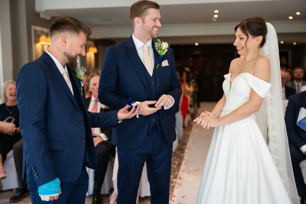 Bride and groom laugh as best man presents rings during their Bull Hotel wedding ceremony.