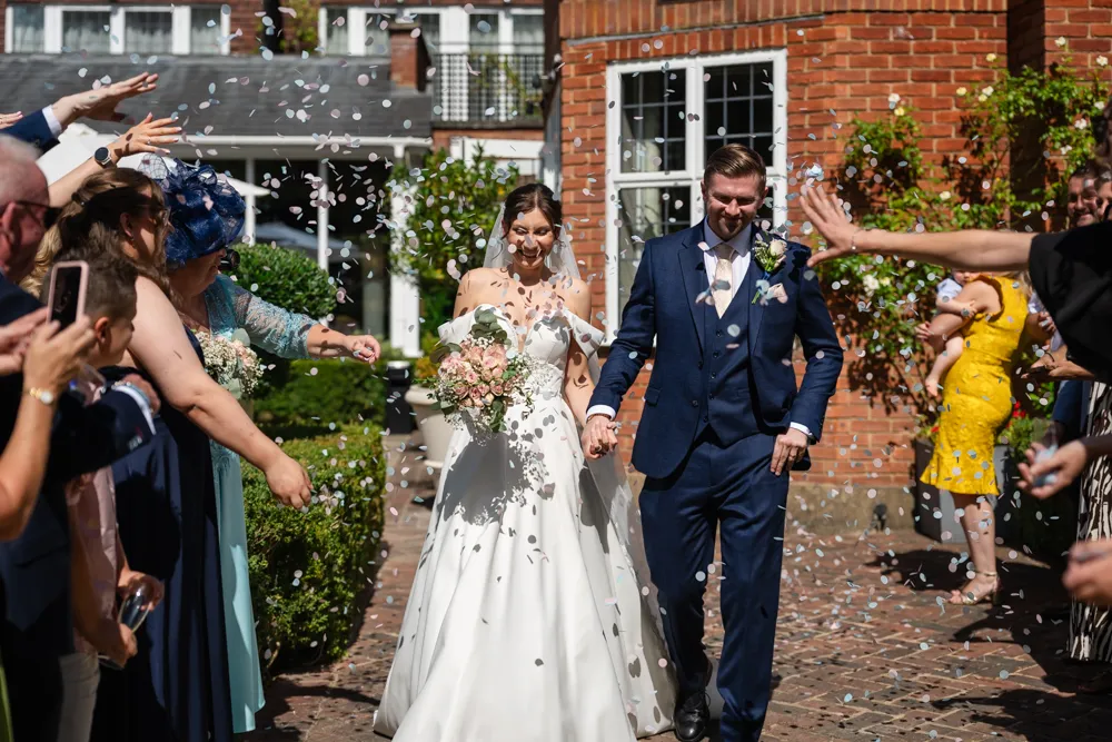 Bride and groom walking though confetti in gardens of Bull Hotel in Gerrards Cross.