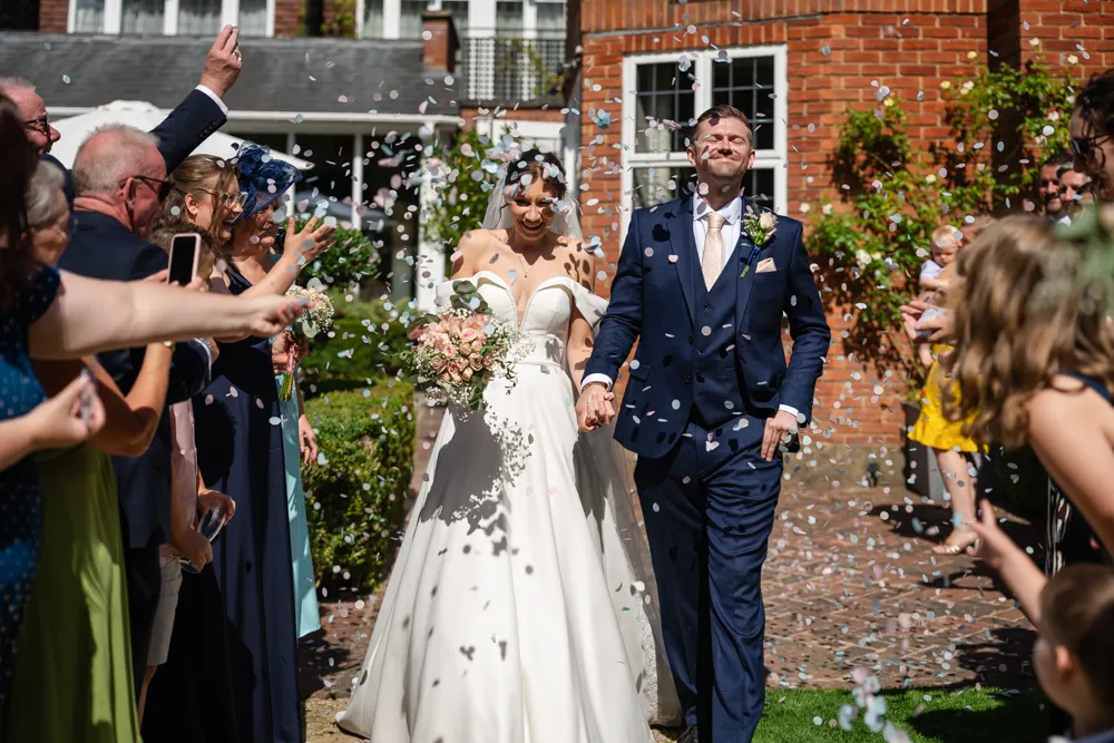 Bride and groom walking though confetti in gardens of Bull Hotel in Gerrards Cross.