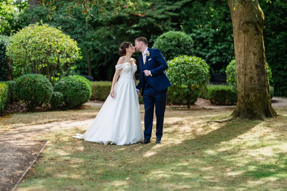 Bride and groom kiss while walking In the gardens of The Bull Hotel in Gerrards Cross on their August wedding day. Bull Hotel Wedding Photographer.