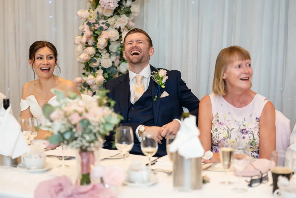 Bride and groom laughing during speech in the Thames Suite. Bull Hotel Wedding Photographer.
