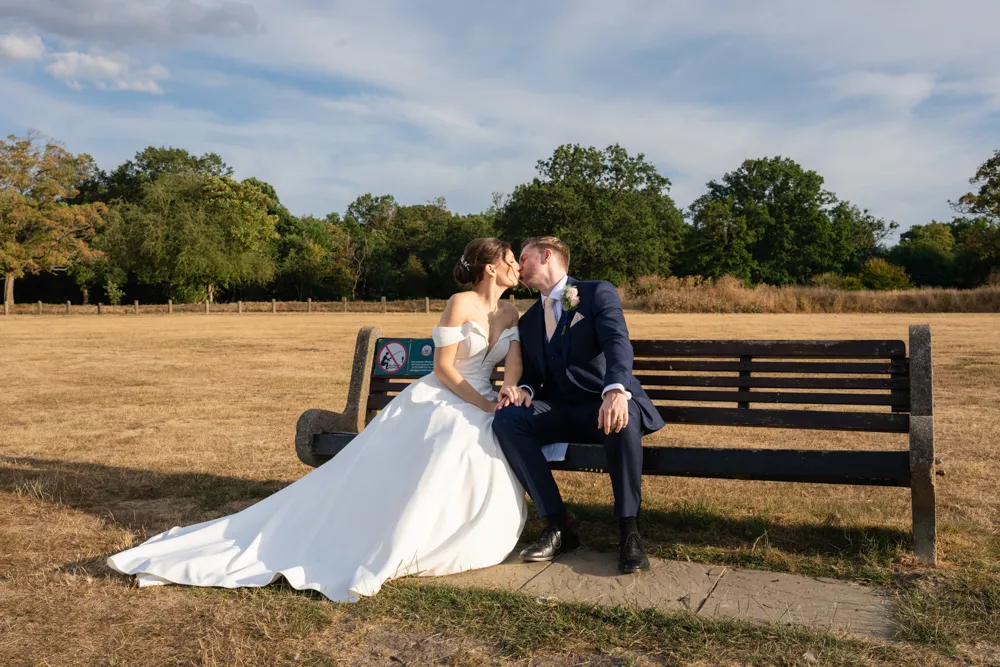 Bride and groom kiss on bench next to Latchmoor pond in Gerrards Cross. Bull Hotel Wedding Photographer.