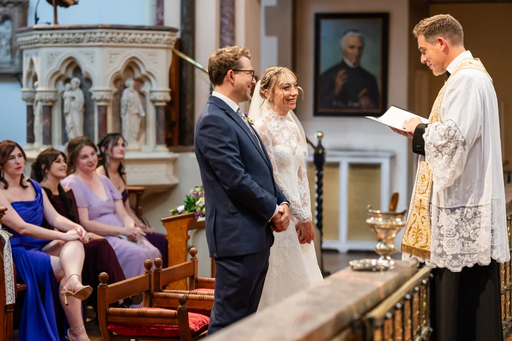 Oxford Oratory wedding photographer. Bride and groom smiling through wedding ceremony.
